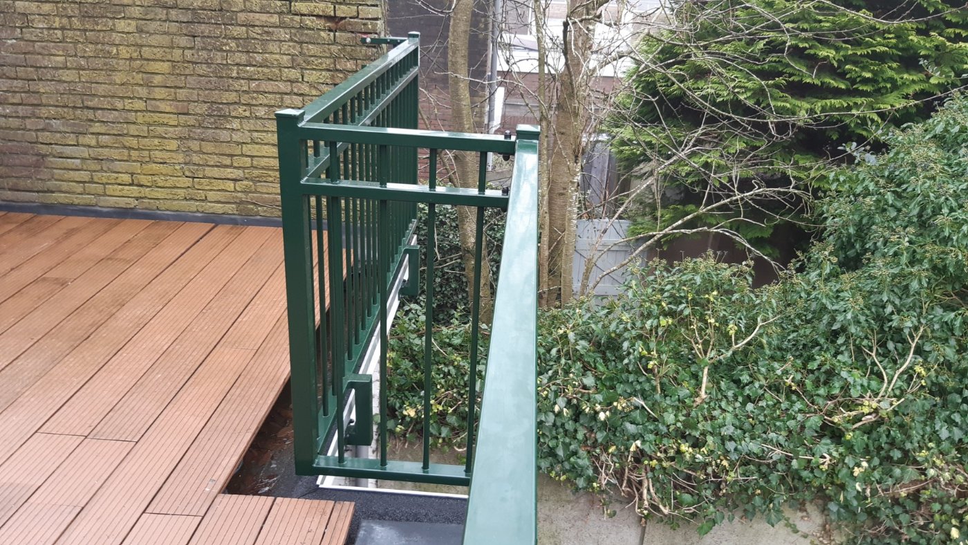 Groene stalen staander van het balkonhekwerk op het hardhouten terras
