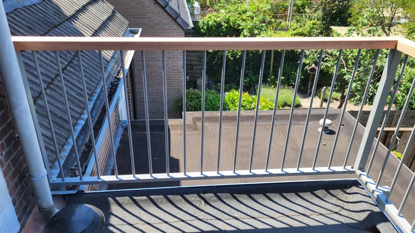 Lichtgrijs spijlenhek met houten bovenregel langs de rand van het dakterras