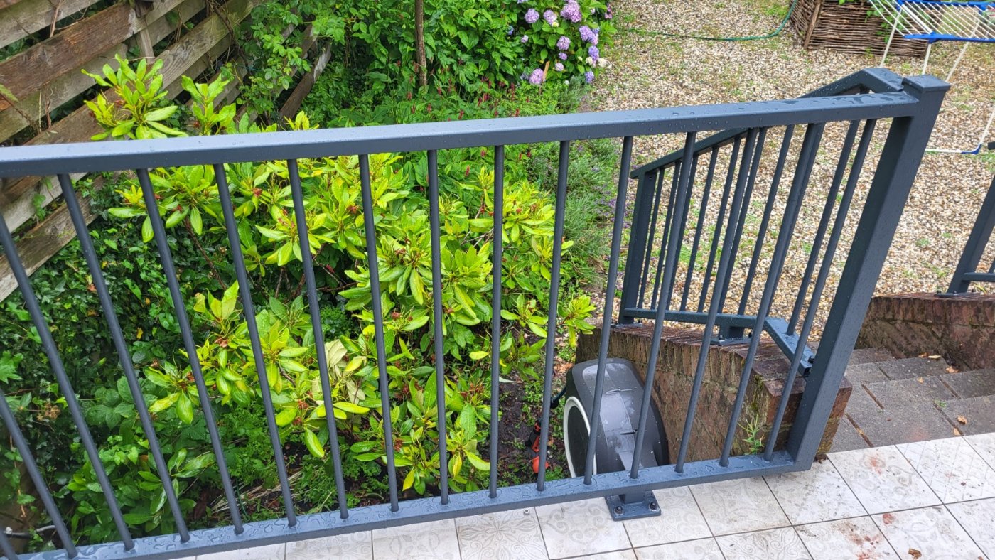 Spijlenhek met voetplaten op het metselwerk en zicht op de lager gelegen tuin