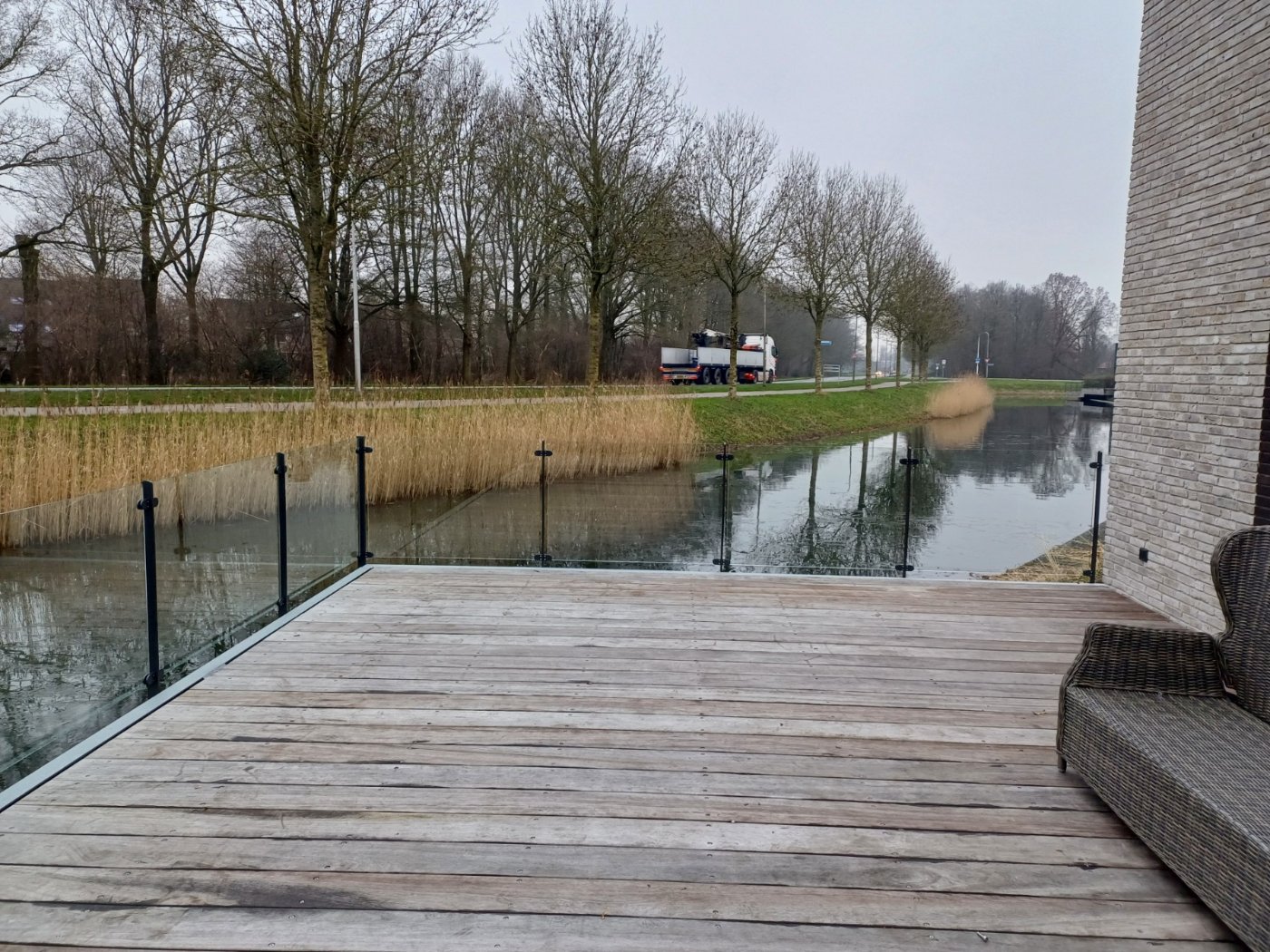 Glazen balustrade met antracietgrijze staanders langs een houten terras aan het water in Biddinghuizen