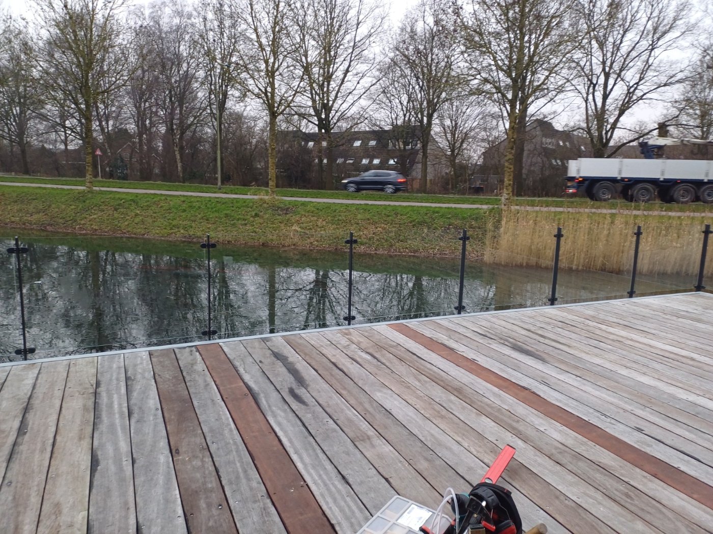 Glazen balustrade met donkere staanders langs de waterkant van het houten terras
