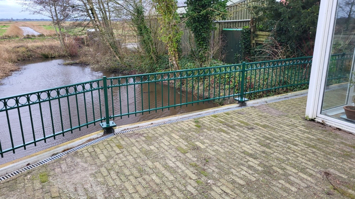 Het sierhekwerk volgt de rand van het bestrate terras langs het water in Hellum