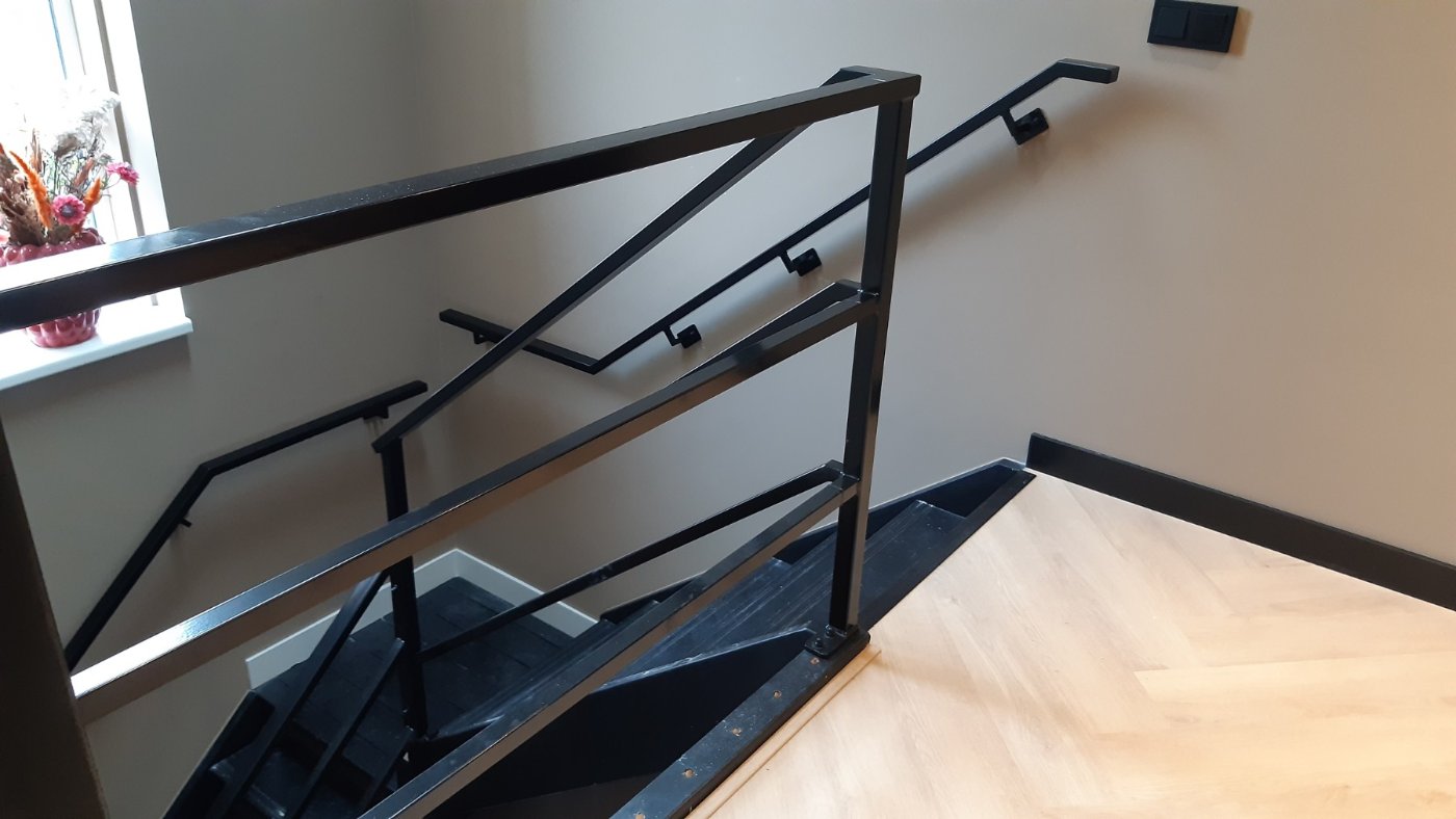 Stalen trapleuning op leuningdragers langs de wand naast de trap